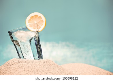 Cold drink with ice and a slice of lemon on the beach on a hot summer day