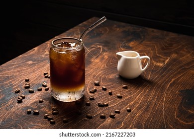 Cold espresso tonic. A highball glass filled with ice cubes, tonic soda water, coffee beans around, wooden background