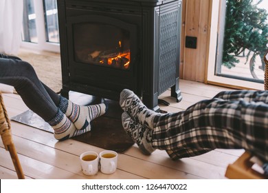 Cold fall or winter day. People drinking tea and resting by the stove. Closeup photo of human feet in warm woolen socks over fire place. Hygge concept of cozy winter weekend in cabin.