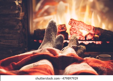 Cold fall or winter evening. People resting by the fire with blanket and tea. Closeup photo of feet in woolen socks. Cozy scene.