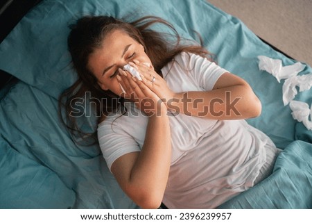 Cold and flue concept. Sick woman suffering from running stuffy nose. Upset ill girl lying in bed, blowing her nose using paper napkin. Copy space. Top view Сток-фото © 