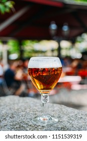 Cold Full Beer Glass On Granite Table With Busy Beer Garden Scene In The Defocused Background