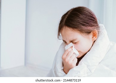 A cold girl blows her nose in a white rag on white background. Rhinitis snot runny nose stuffy nose. Allergy Preteen girl with handkerchief. medical concept