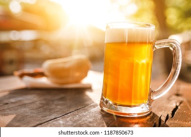 Cold Glass Mug Of Beer With Foam With Bratwurst Hotdog With Sun Beams