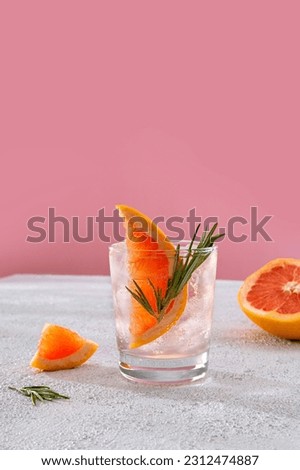 Cold grapefruit cocktail with slices of fresh grapefruit decorated twig rosemary.  Sunny day shadows.  A refreshing summer mocktail