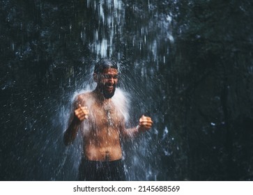 Cold but great. Shot of a young man standing under a waterfall being completely soaked in water but loving every moment of it.