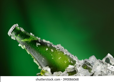Cold green bottle of beer with water droplets and ice cubes over green background
