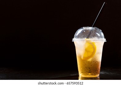 Cold Iced Tea With Lemon And Straw In Takeaway Plastic Cup On Dark Background