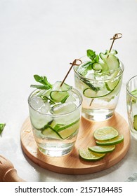 cold infused cucumber water in glasses with ice, lime and thin slices of cucumber skewered. Close-up view with gray background.