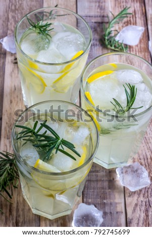 Cold lemon drink with rosemary, ice and tonic, on rustic wooden table. Selective focus
