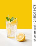 A  cold lemonade in a glass with lemon, mint and ice on a yellow and white background. The concept of a refreshing and healthy drink on a summer day. Copy space.