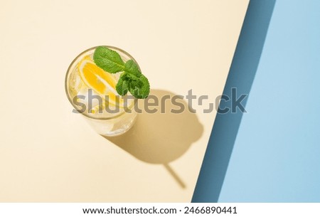 Cold lemonade in a glass with lemon, mint and ice on a yellow blue background  with shadow. Refreshing and healthy drink concept. Top view and copy space..