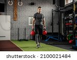 Cold look and focus on training. Adult muscular man in sportswear carries around weights in his hands and walks lightly through the gym. Good figure and body position, complete commitment to training