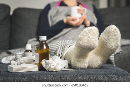 Cold medicine and sick woman drinking hot beverage to get well from flu, fever and virus. Dirty paper towels and tissues on table. Ill person wearing warm woolen stocking socks in winter.  - Shutterstock ID 650188465