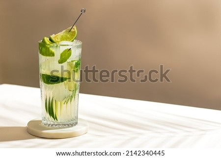 cold Mojito cocktail with rum, lime, ice cubes and mint. Tropical palm leaf shadow. Sunlight and shadow background. beige minimal