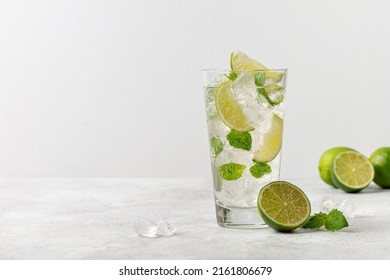 Cold mojito, lemonade with ice, lime and mint on grey background, fresh summer tonic in glass. Cold drink. Copy space