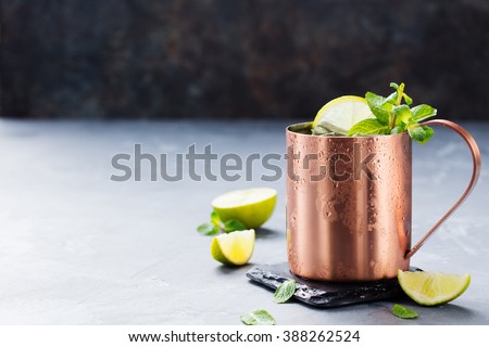 Cold Moscow Mules cocktail with ginger beer, vodka, lime. Grey stone background. Copy space.
