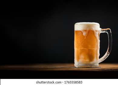 cold mug with beer, with overflowing foam, on wooden table and dark background wish space - Powered by Shutterstock