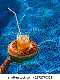 Cold refreshing drink with ice and a straw in the inflatable ring in shape of watermelon in a woman's hand in a pool of blue water. Concept of summer holiday in hotel or pool party. Copy space - Shutterstock ID 2172770321