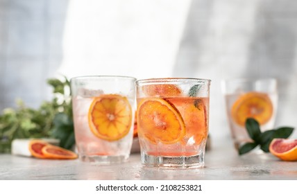 Cold refreshing drink with tonic, blood Sicilian oranges and ice, grey background. Cocktail with tonic and oranges. Direct sunlight and hard shadows.