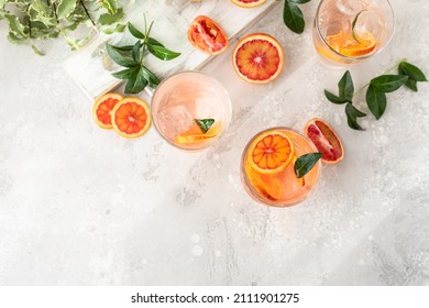 Cold refreshing drink with tonic, blood Sicilian oranges and ice, grey concrete background. Cocktail with tonic and oranges. Top view.