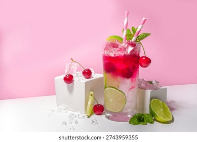 Cold and refreshing summer drink. Cherry cola, limeade, mojito lemonade cocktail with lime and cherries on colorful bright pink background