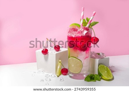 Cold and refreshing summer drink. Cherry cola, limeade, mojito lemonade cocktail with lime and cherries on colorful bright pink background