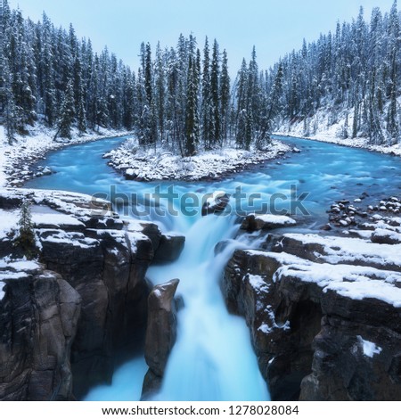 Cold scenery at Sunwapta Falls in the Canadian Rockies with snow and fir trees in wonderful scenery and ice and blue rivers running through the scenery with snowy hut.First snow in Jasper national 