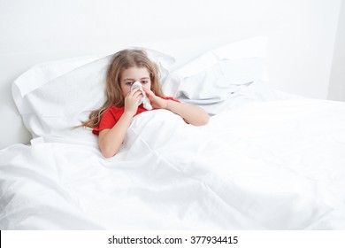 cold sick child laying on bed and blowing her nose in tissue - Powered by Shutterstock