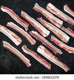 Cold Sliced Bacon On Black Table Grunge Background, Overhead View. Streaky Fresh Bacon Top View.