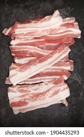 Cold Sliced Bacon On Black Table Grunge Background, Overhead View. Streaky Fresh Bacon Top View.