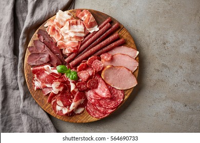 Cold smoked meat plate with prosciutto, salami, bacon, pork chops, cheese and olives on gray stone background. From top view