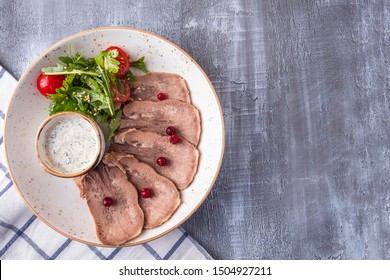 Cold snack with sliced beef tongue, salad and white sauce. Top view. Copy space