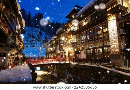 A cold snowy winter evening in Ginzan Onsen 銀山温泉, a famous hot spring resort in Obanazawa, Yamagata, Japan, with bridges over a river flanked by historic wooden buildings dating back to Taisho Era 商業照片 © 