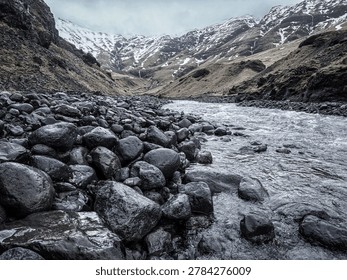 Cold stream flows through a rocky valley with snow on distant mountains
