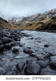 Cold stream flows through a rocky valley with snow on distant mountains