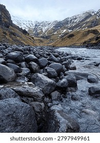 Cold stream flows through a rocky valley with snow on distant mountains