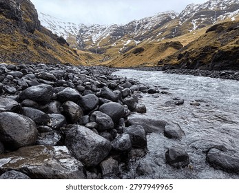 Cold stream flows through a rocky valley with snow on distant mountains