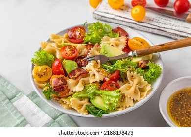 Cold summer pasta salad with bacon, tomatoes, avocado and mustard in a plate with fork on white background. Healthy diet food - Powered by Shutterstock