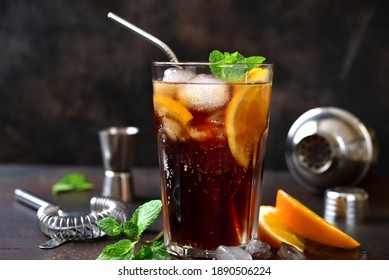 Cold summer soda cocktail with cola, dark rum and orange in a tall glass on a dark slate, stone or concretebackground.