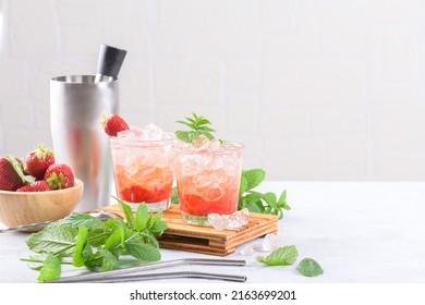 Cold summer strawberry cocktail mojito, margarita, daiquiri. Two glasses with fresh strawberry soda drink, ice cubes, mint and bartender tools on light background. Iced strawberry lemonade, copy space
