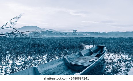 Cold swamp tranquil scene with wooden boat floating on Rawa Pening lake surrounded by lush vegetation, with Mount Ungaran background - Powered by Shutterstock