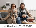 Cold symptom. Couple with cups of drink suffering from fever on sofa at home