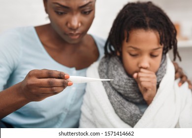 Cold Symptoms. Worried Black Mother Looking At Thermometer, Ill Daughter Coughing. Selective Focus