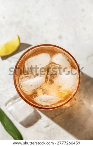 Cold tea in a glass with lime slice and ice cubes close up on white background. Refreshing iced summer drink, top view. Vertical