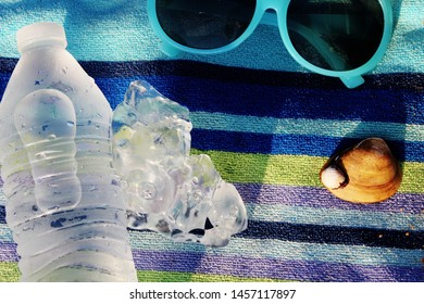 Cold Water, Ice, Shell And Sunglasses Against A Blue Towel In A Flat Layout