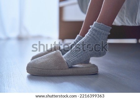 Cold weather. Children's feet in warm socks and slippers. Early in the morning a young girl puts on slippers after sleeping. Comfort and relaxation in the cold season concept