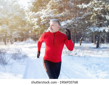 Cold Weather Running Concept. Fit Mature Man In Sports Clothes Jogging At Snowy Winter Park. Healthy Senior Sportsman Getting Ready For Race Or Marathon In Frosty Forest. Seasonal Workout