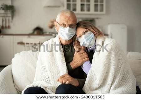 Cold winter, elderly husband and wife wearing protective face masks at home