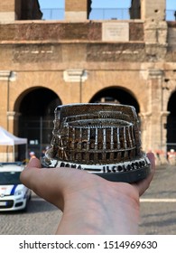 Coliseum Toy Souvenir On Woman's Hand Across Real Coliseum Building